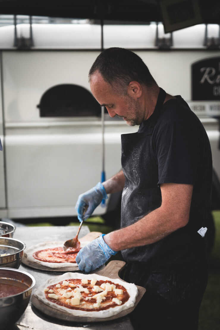 Chef preparing pizzas with sauce and cheese.