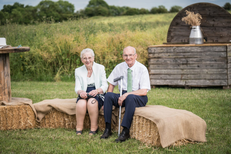 Elderly couple sitting on hay bales outdoors.