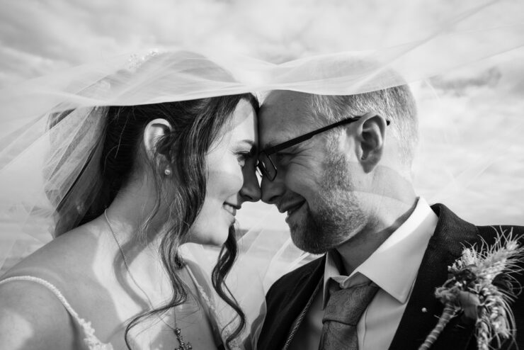 Smiling couple close under wedding veil