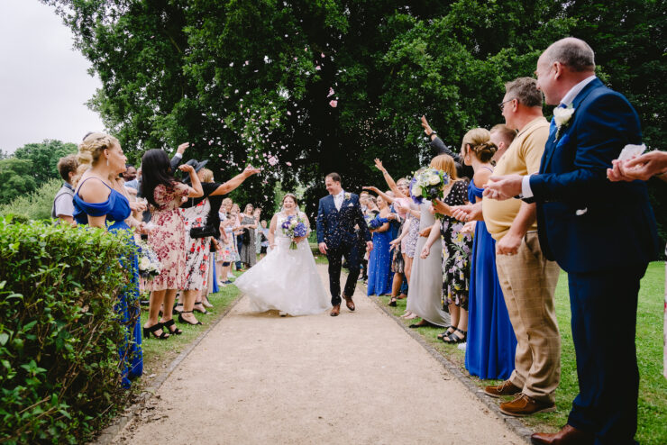 Bride and groom walk through confetti in garden wedding.
