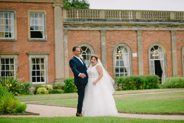 Bride and groom laughing outside large brick building.