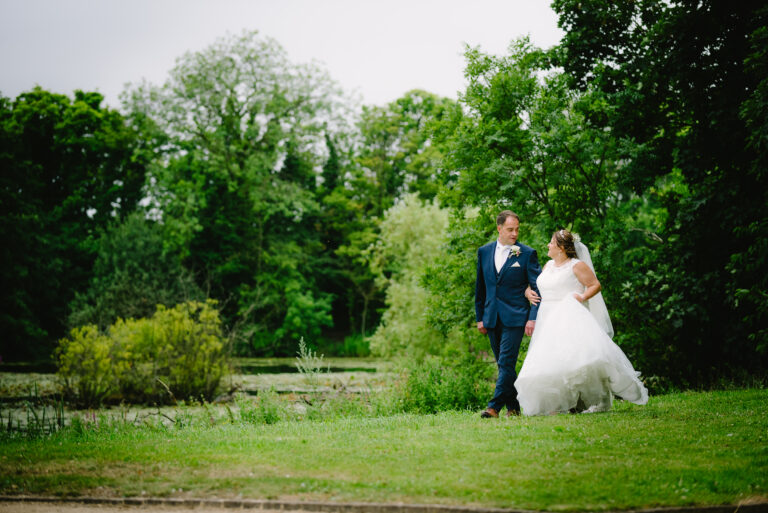 Bride and groom walk in lush green park.