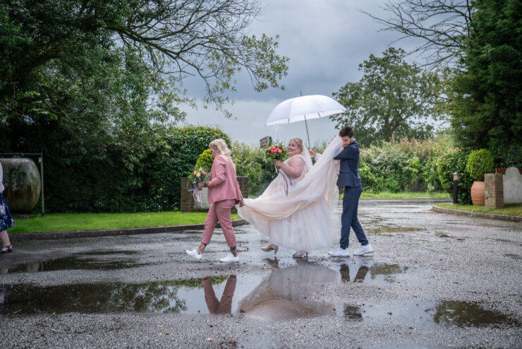 Bride walking with umbrella on a rainy wedding day.