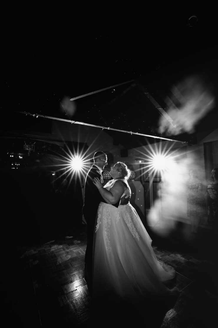 Couple dancing at wedding under bright lights.