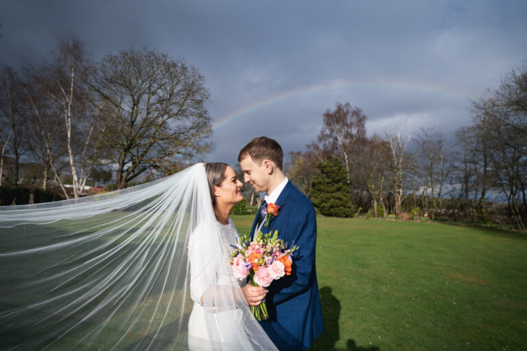 Bride and groom under rainbow on wedding day.
