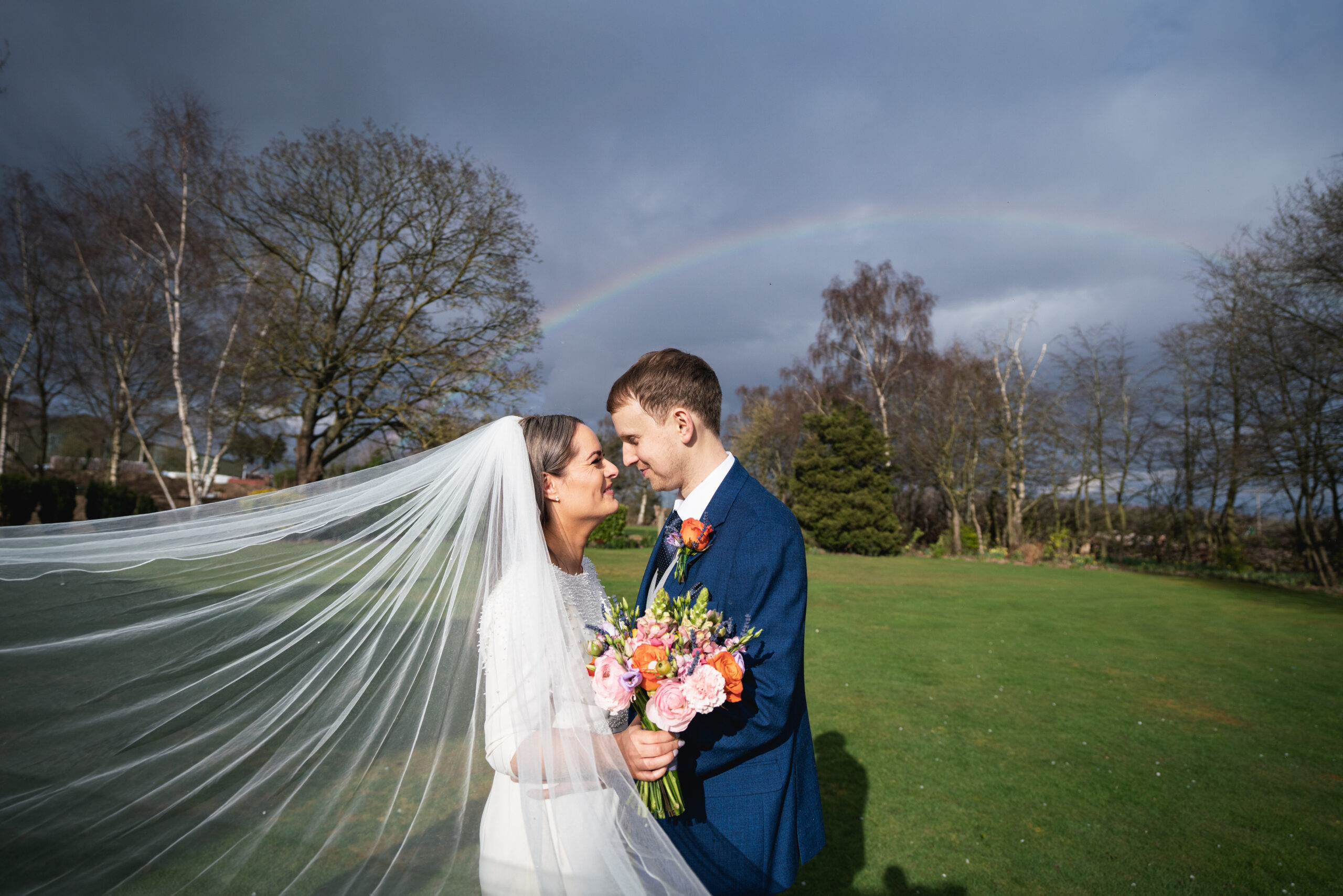 Bride and groom under rainbow on wedding day.