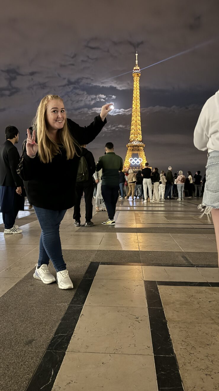 Woman posing near illuminated Eiffel Tower at night.