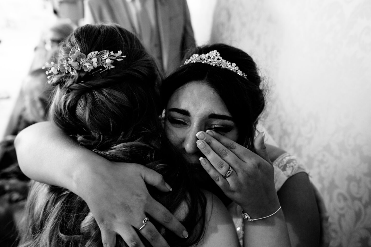 Bride embraces emotional woman at wedding.