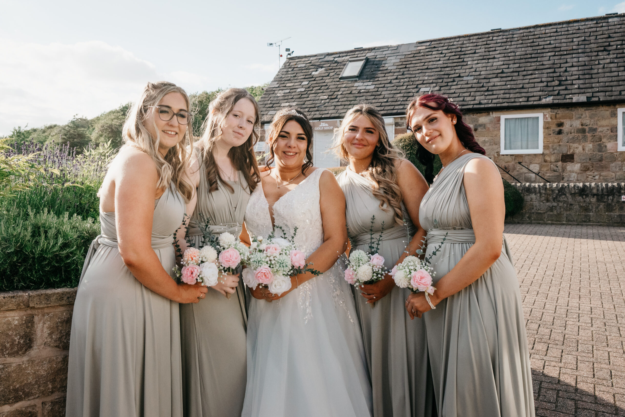 Bride with bridesmaids holding bouquets outdoors.