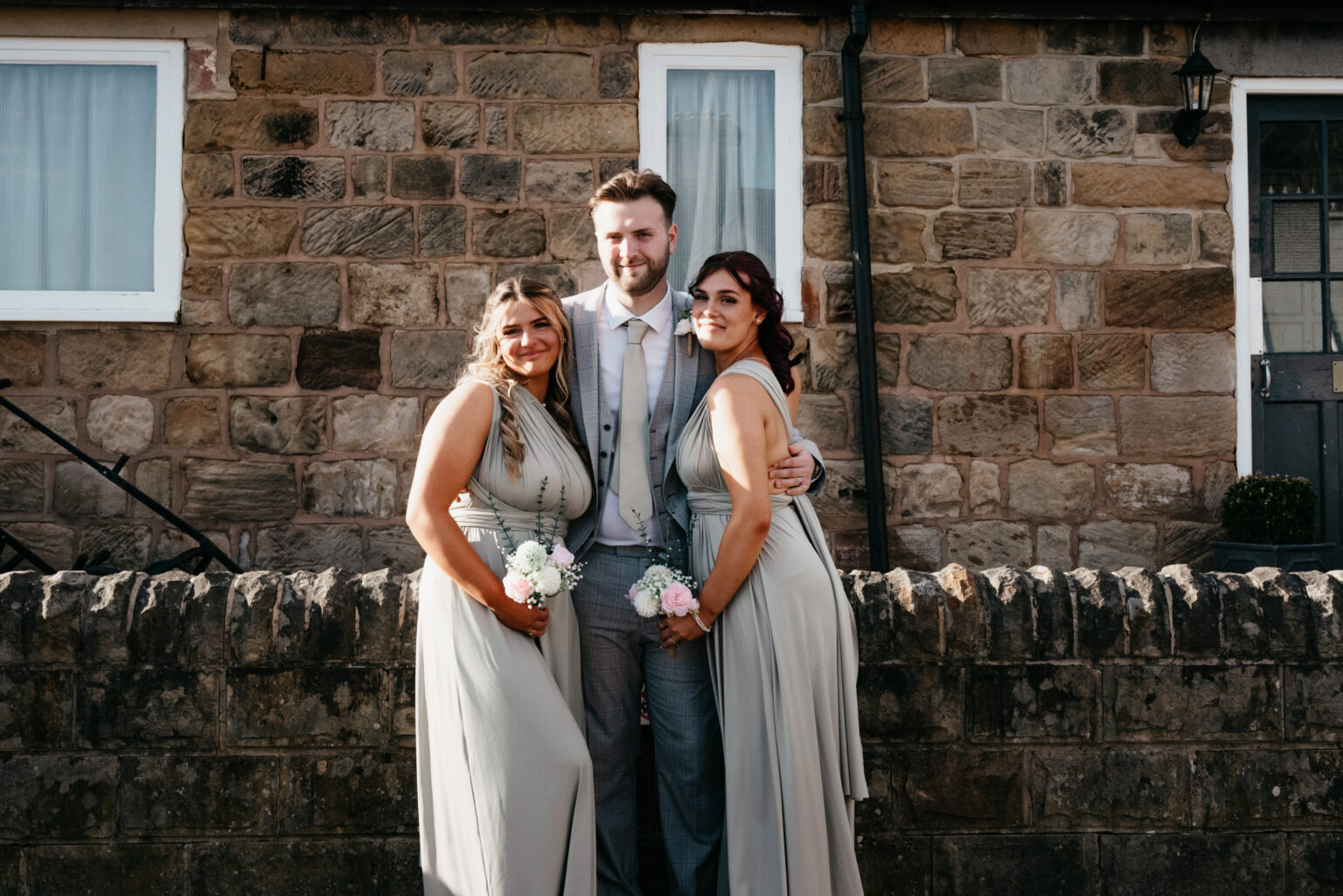 Wedding photo: two bridesmaids, groom in front of cottage.