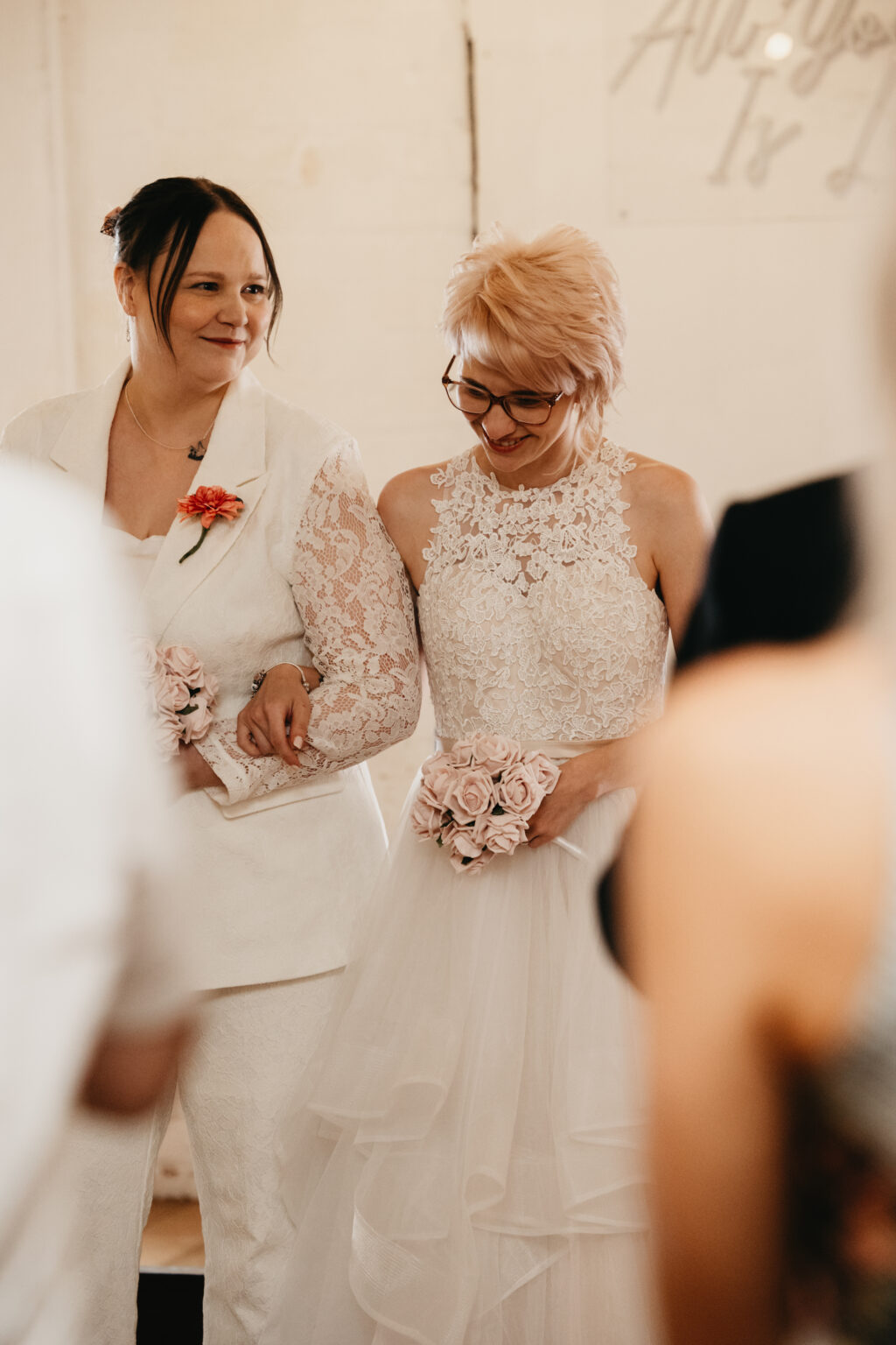Two brides smiling arm-in-arm, holding bouquets.