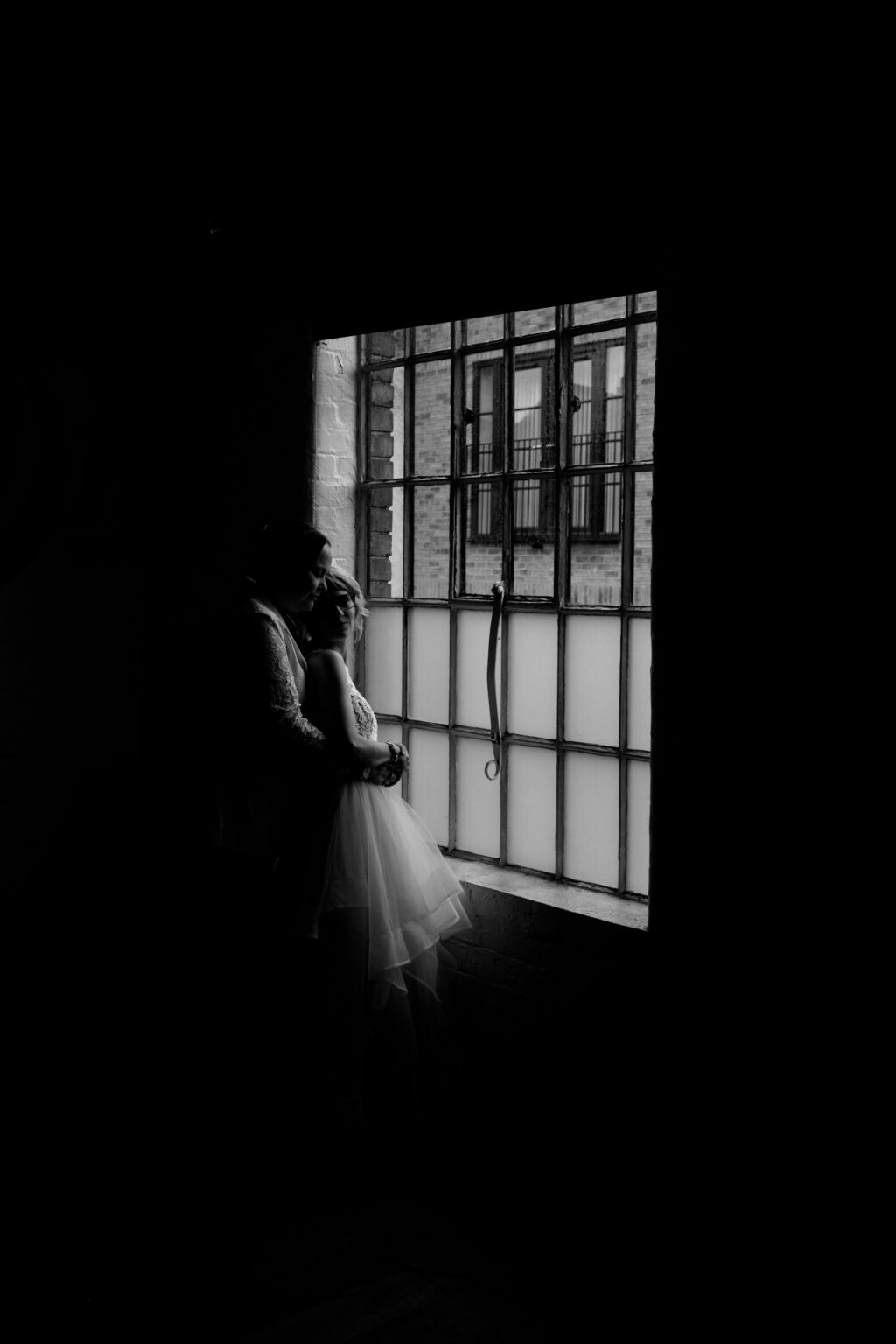 Couple embraces by window, black and white photograph.