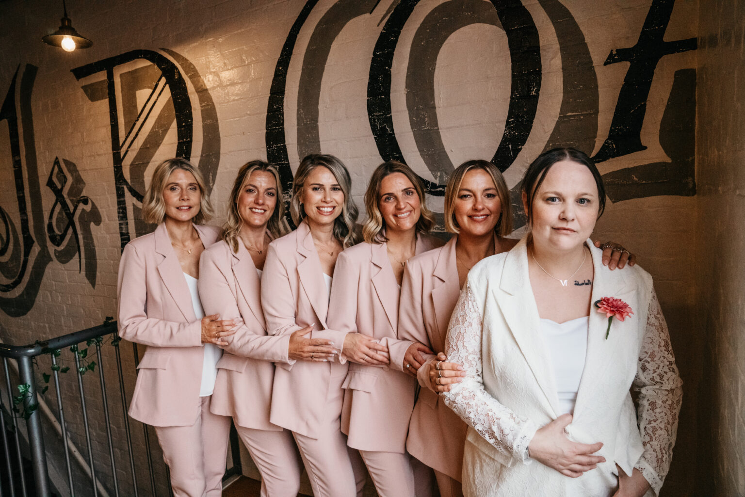 Seven women in matching suits, smiling together indoors.