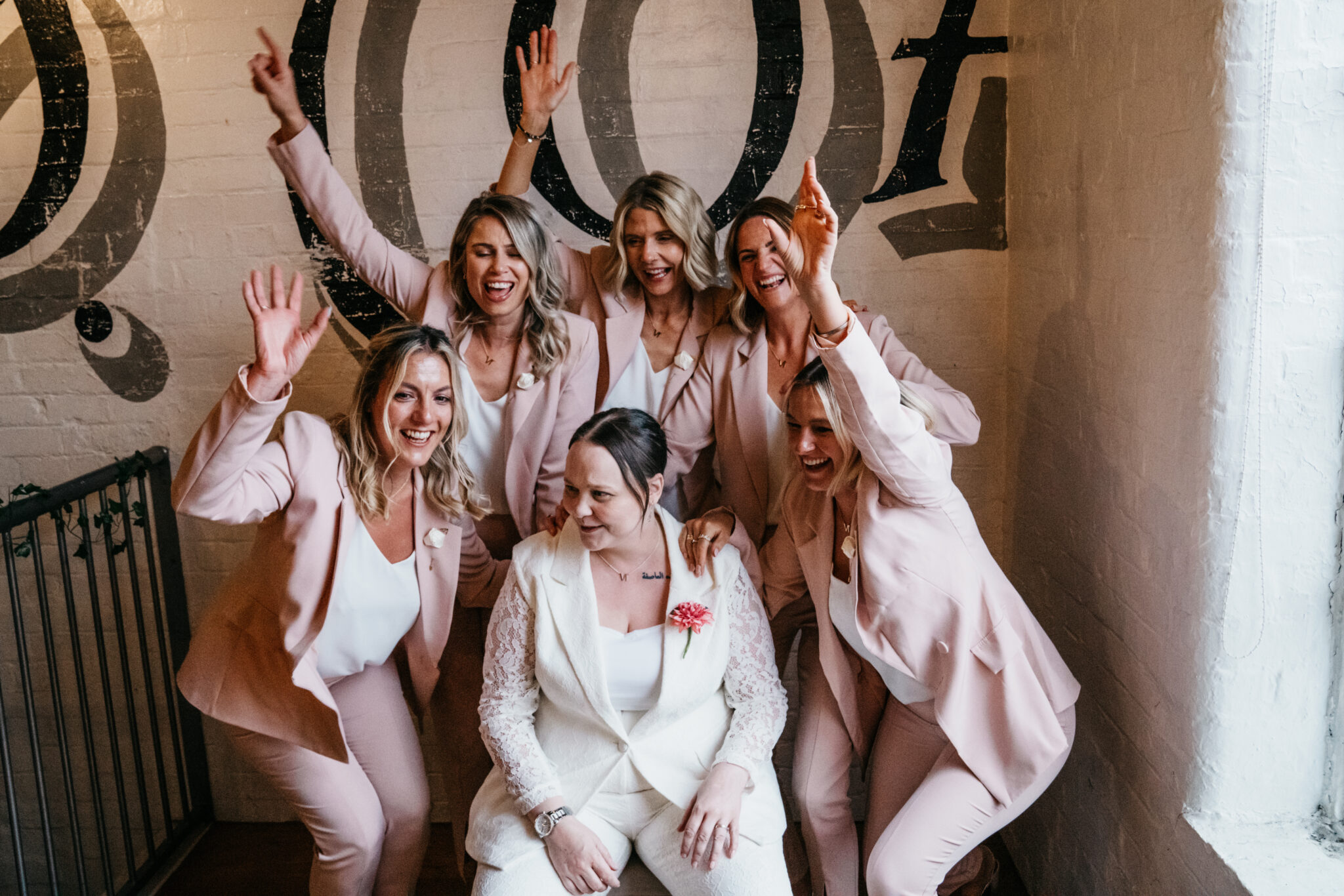 Women celebrating in pink suits and white outfit.