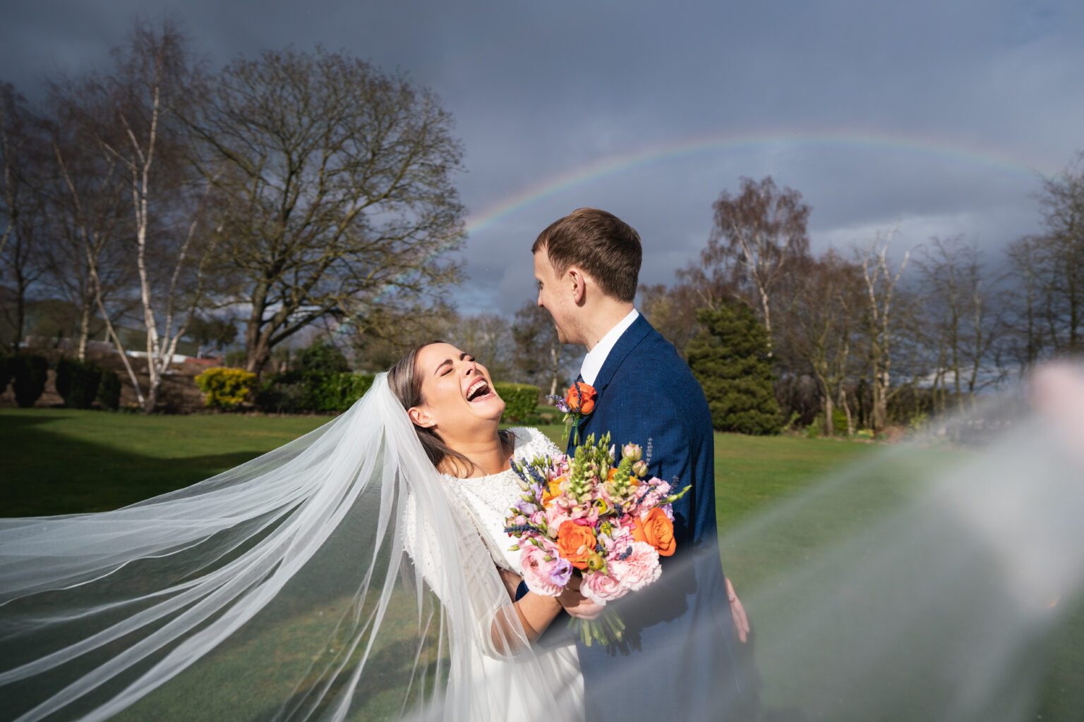 Bride and groom laughing under a rainbow