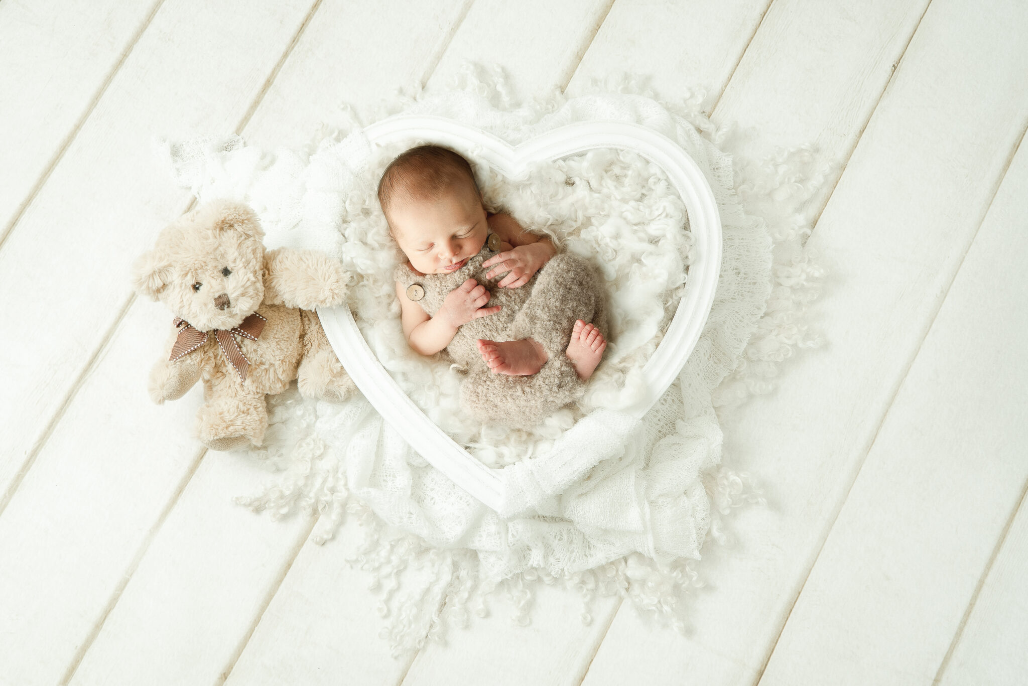 Sleeping baby in heart frame with teddy bear.
