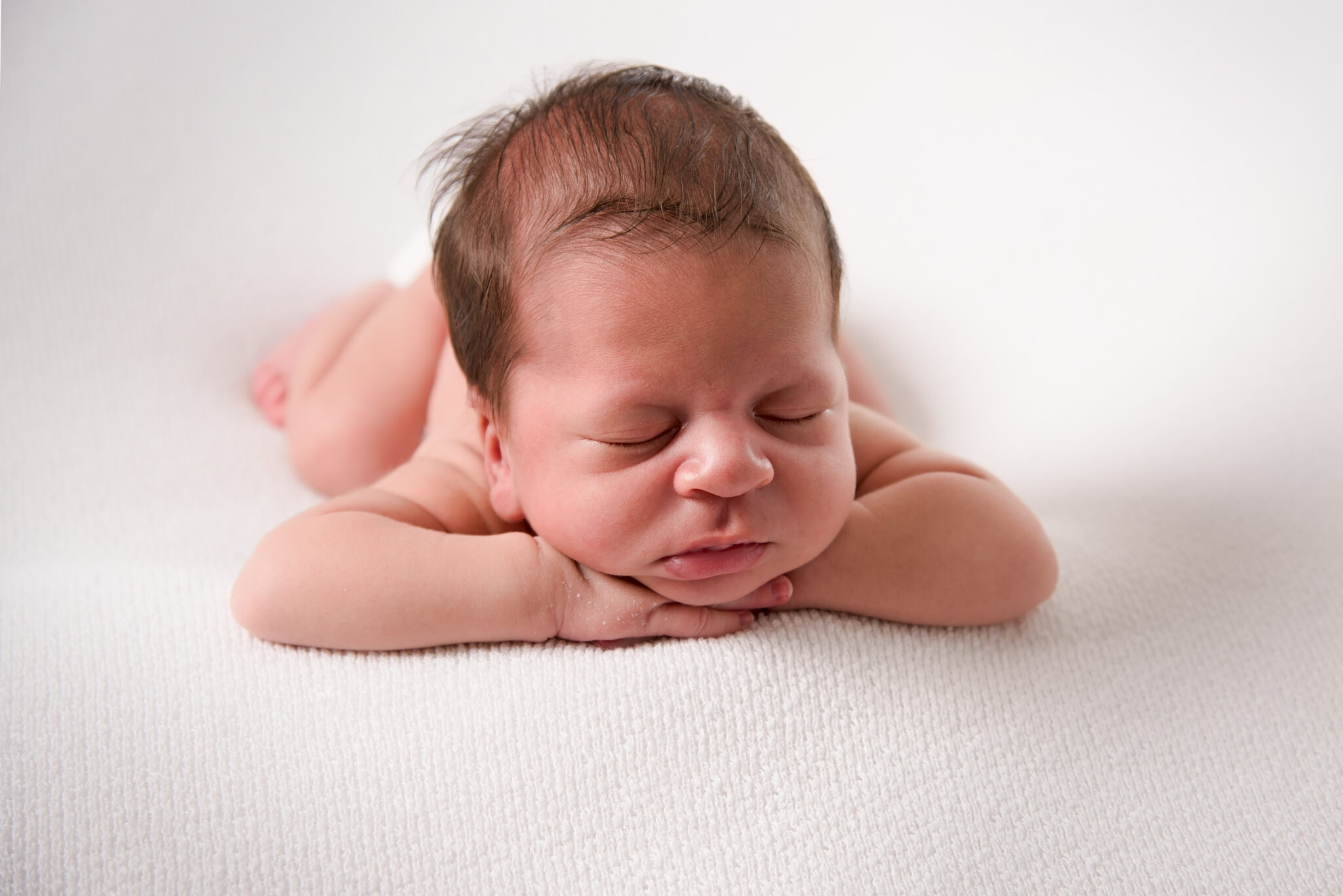 Sleeping newborn baby on soft white blanket.