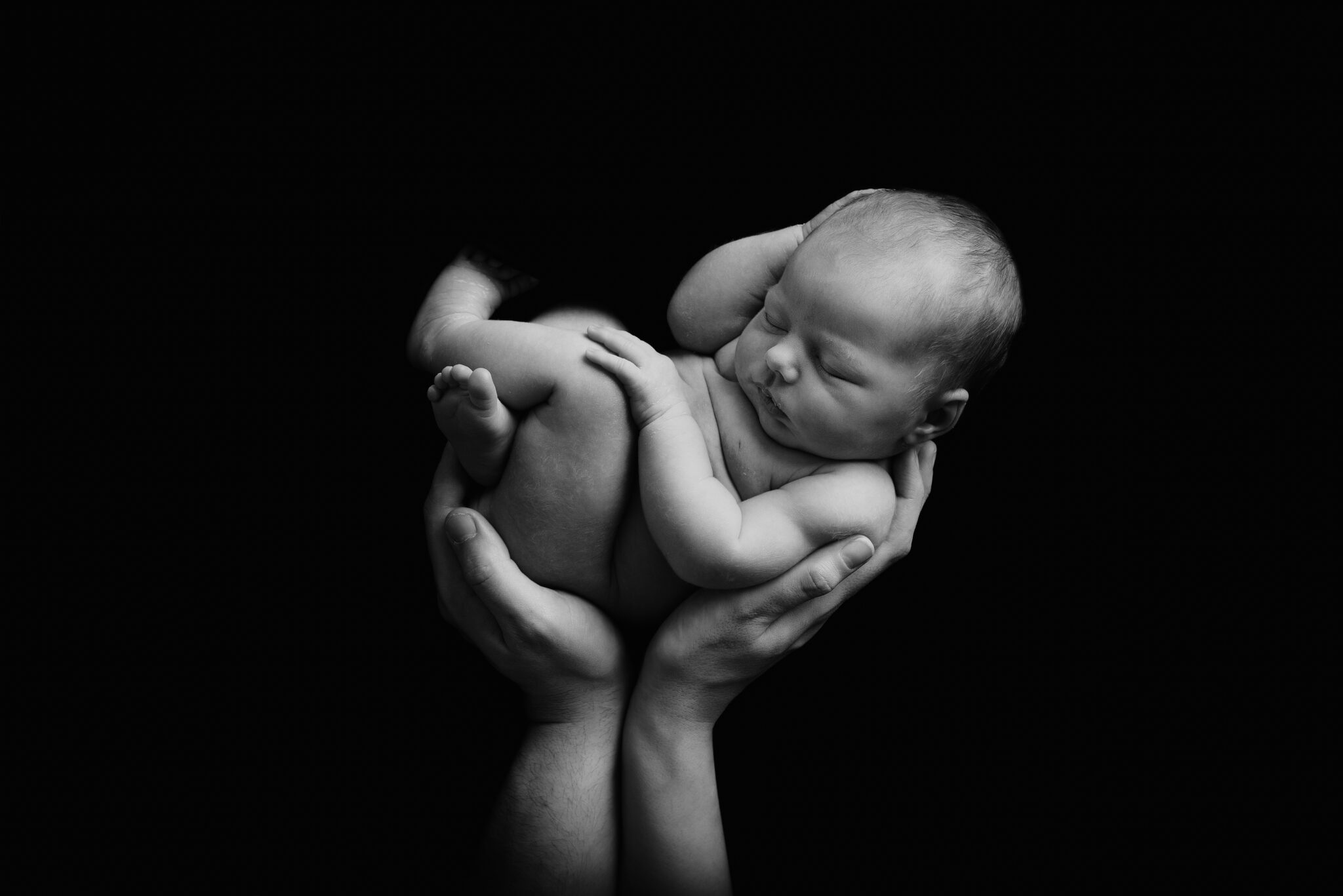 Newborn baby cradled in hands, black background.
