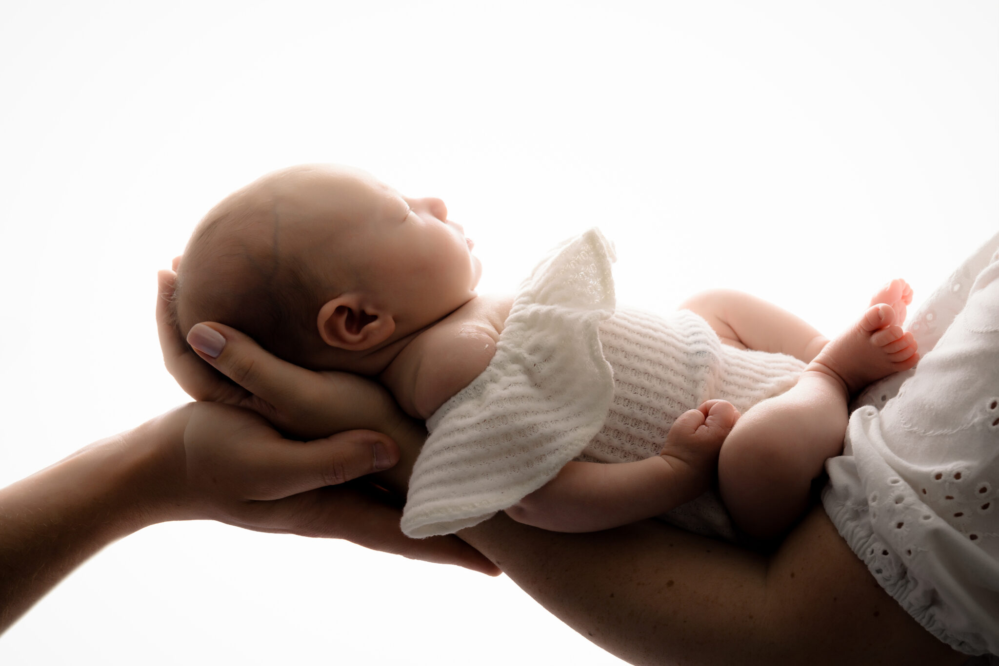 Person cradling sleeping baby wrapped in white blanket.
