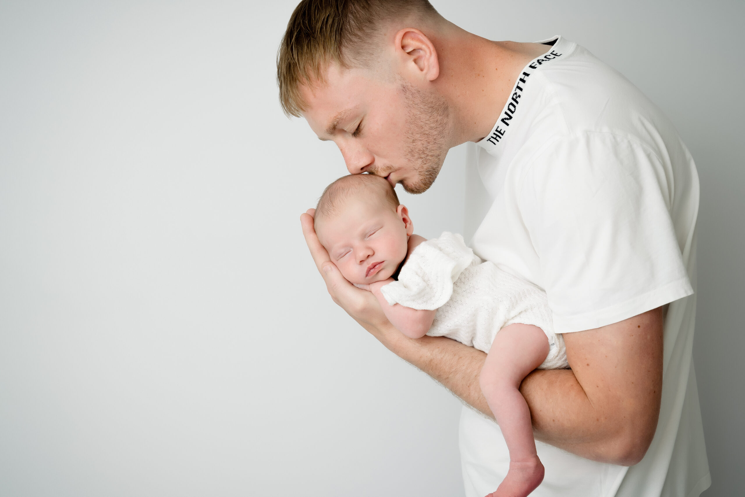 Man kissing sleeping baby on cheek.