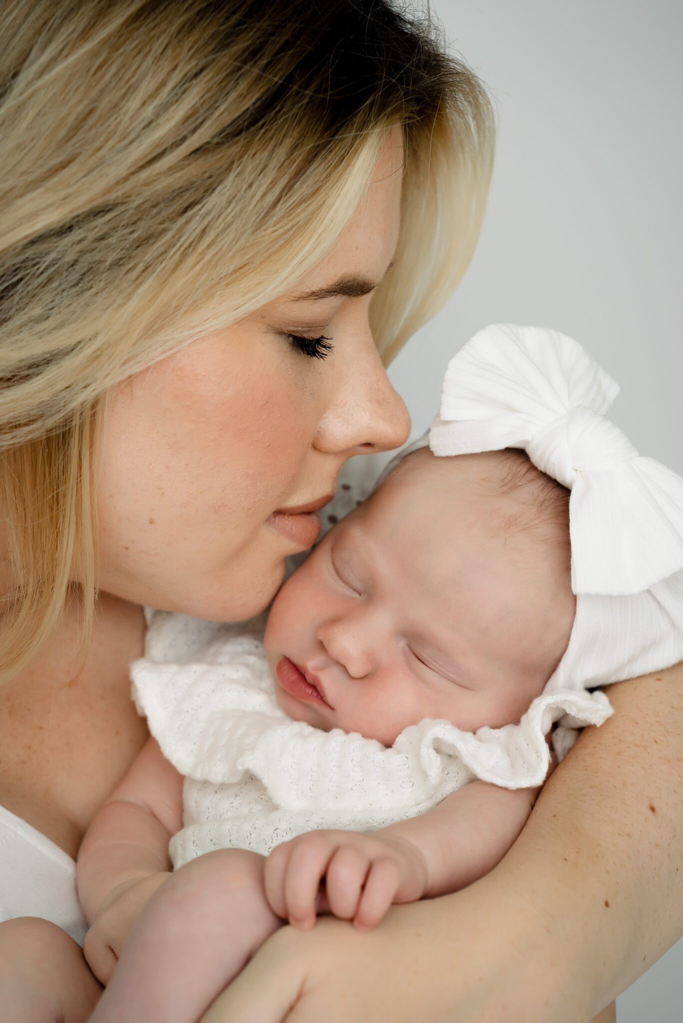 Mother cuddling sleeping baby with white bow.