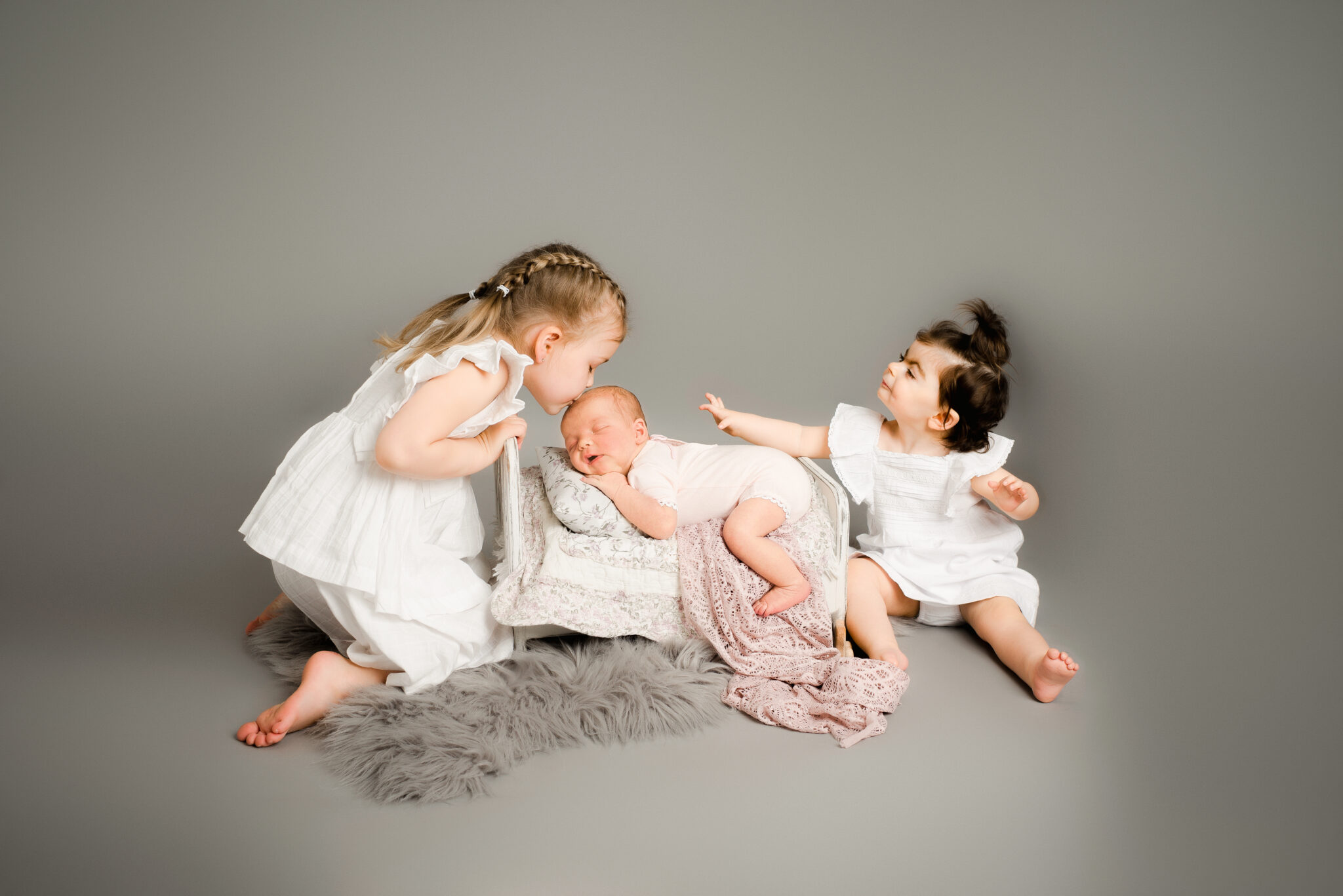 Three children, two sitting, one kissing baby.