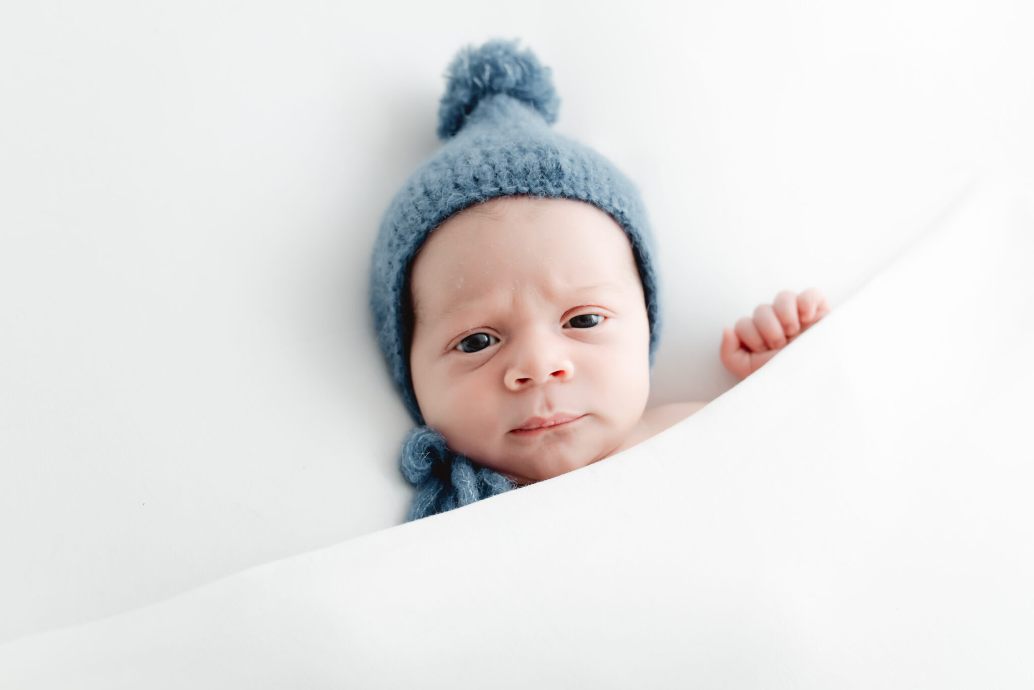 Baby in blue hat under white blanket.