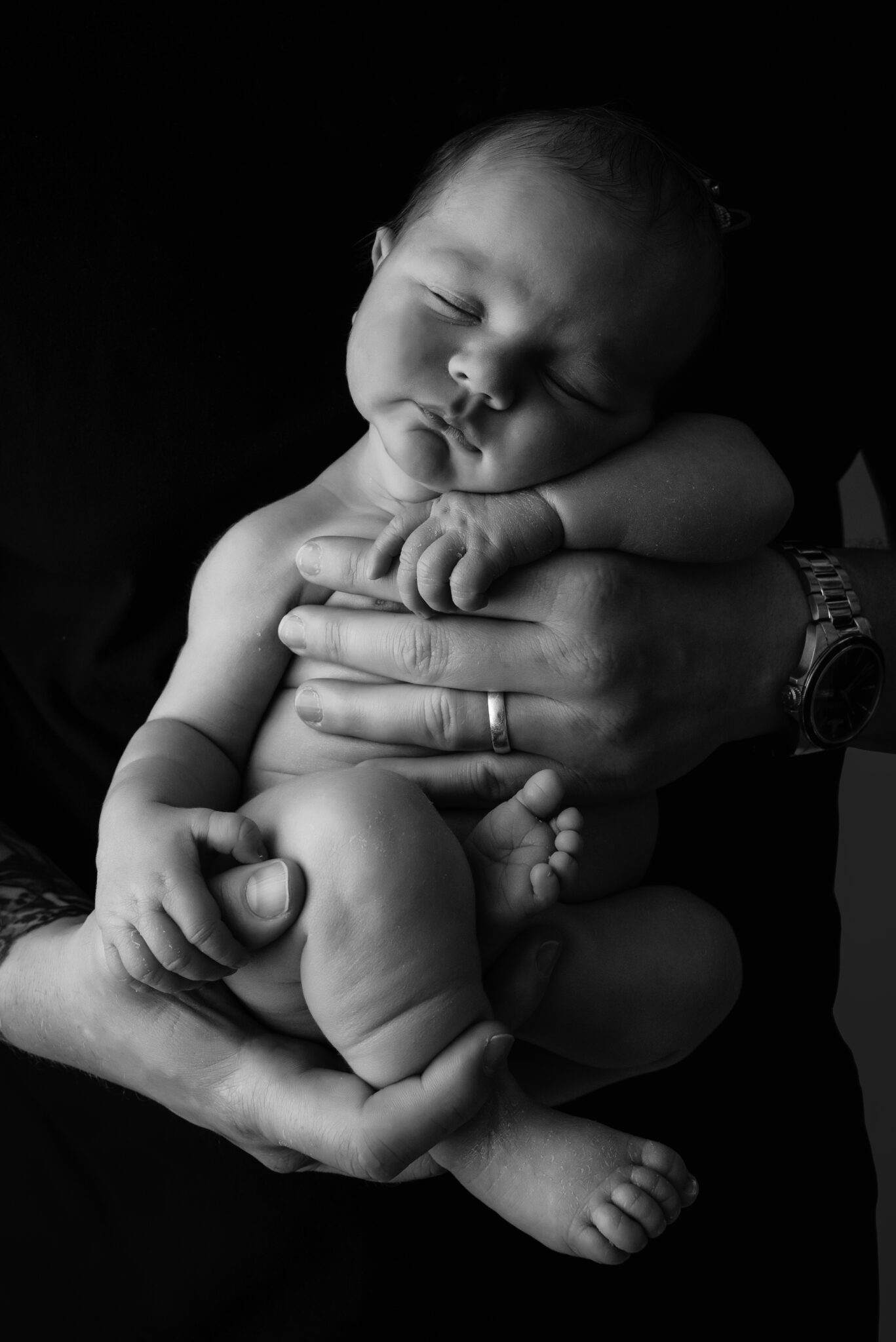 Sleeping baby embraced in adult hands, monochrome portrait.