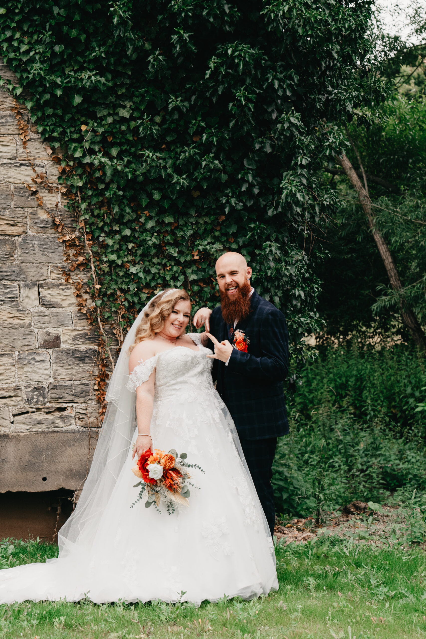 Bride and groom smiling outdoors near ivy-covered wall.