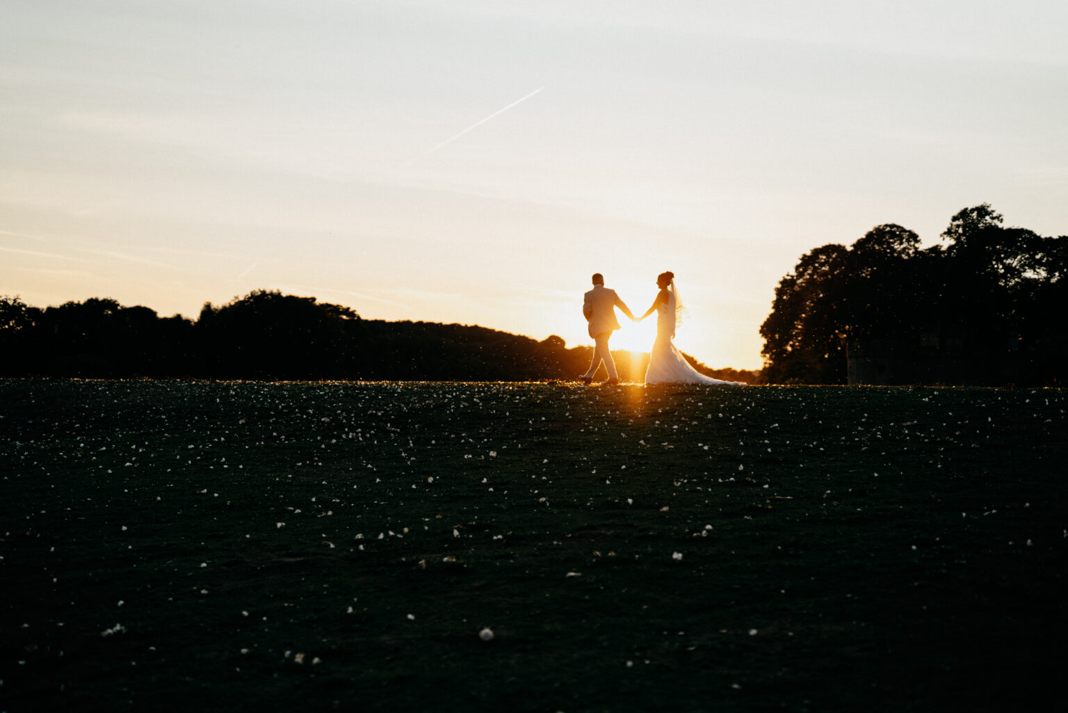 Couple holding hands at sunset in a field.
