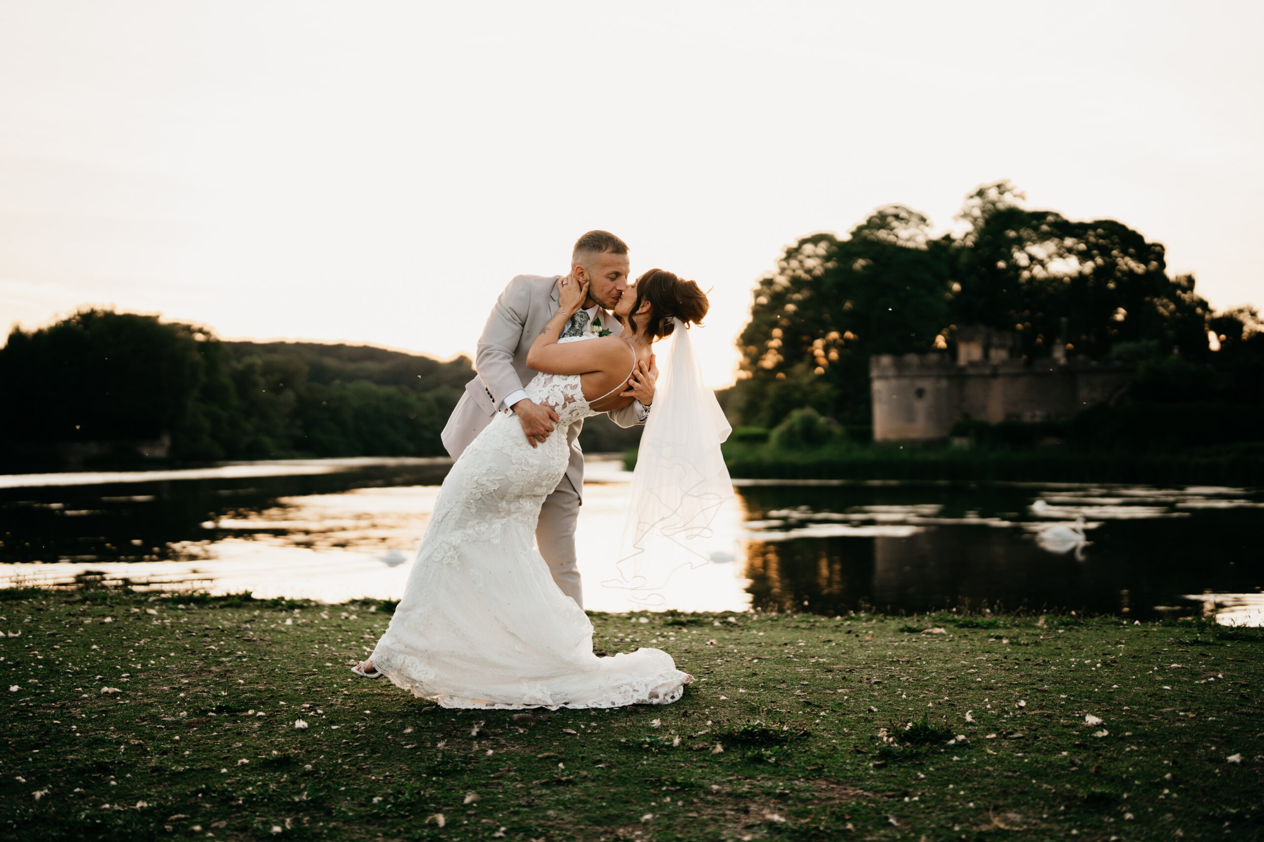 Bride and groom kiss by lakeside at sunset