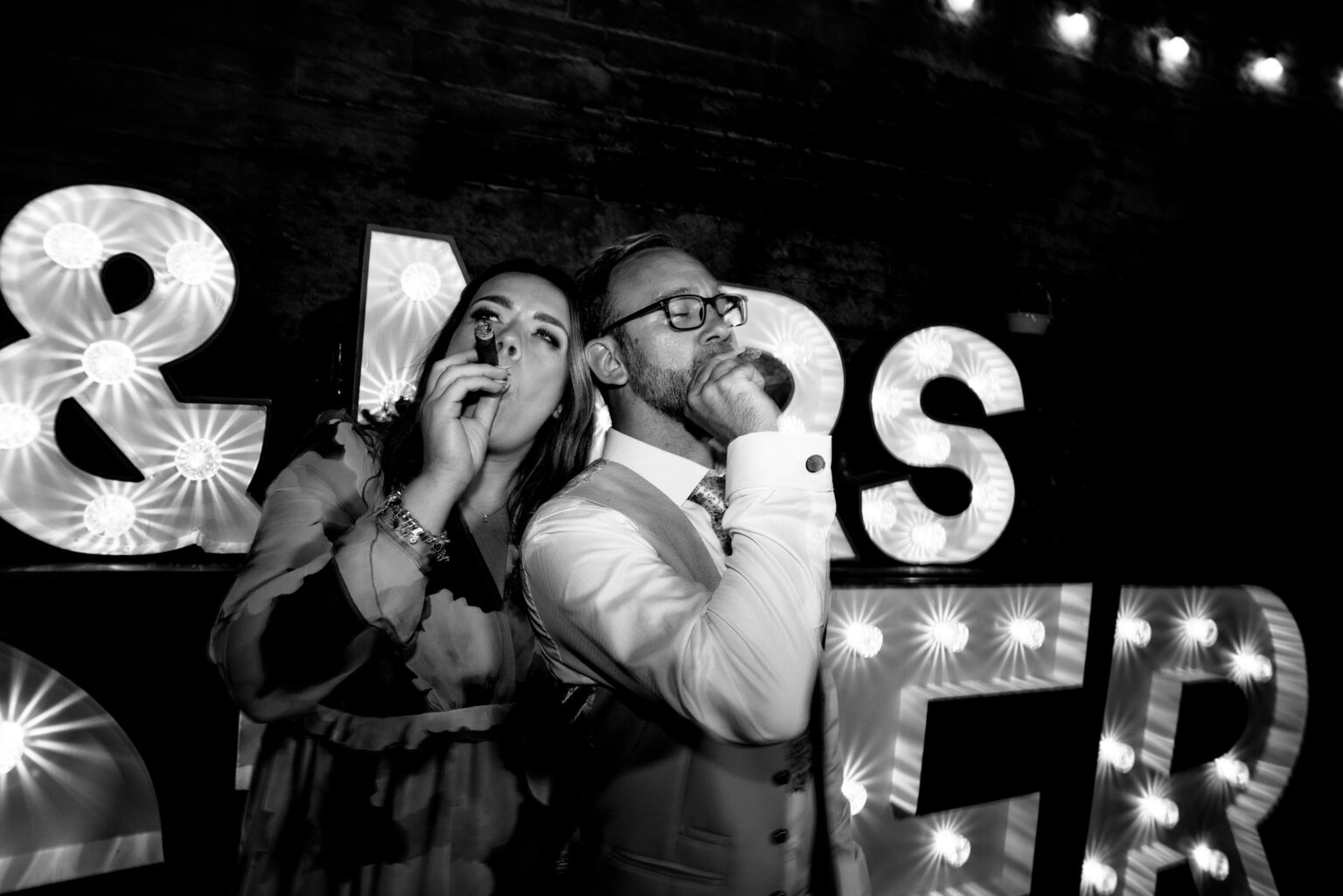 Two people celebrate with cigars at night event.