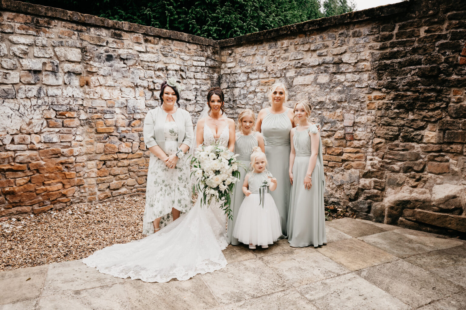 Bride with bridesmaids in courtyard, dressed in pastel gowns.