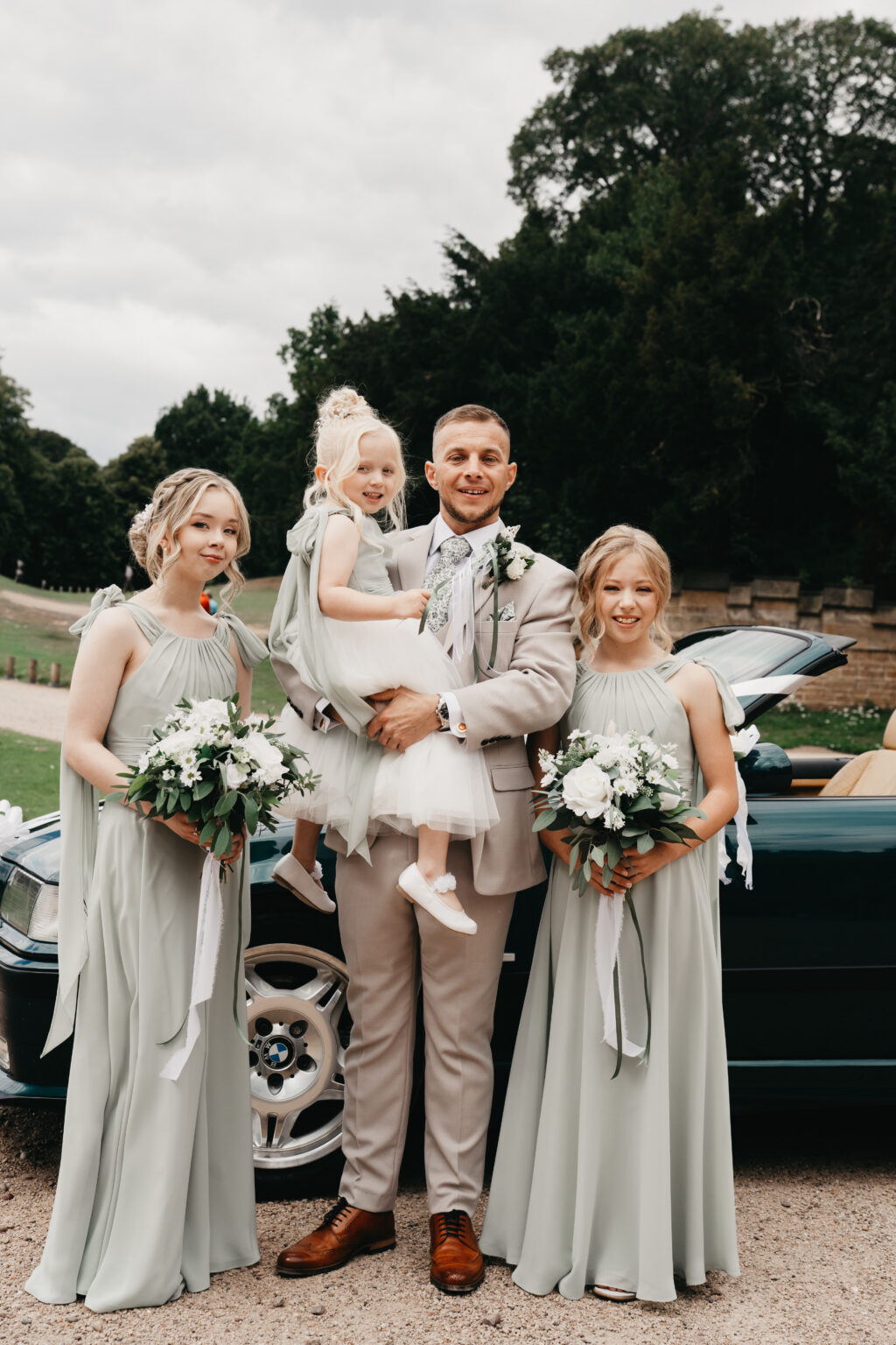 Wedding party posing outdoors with a car.