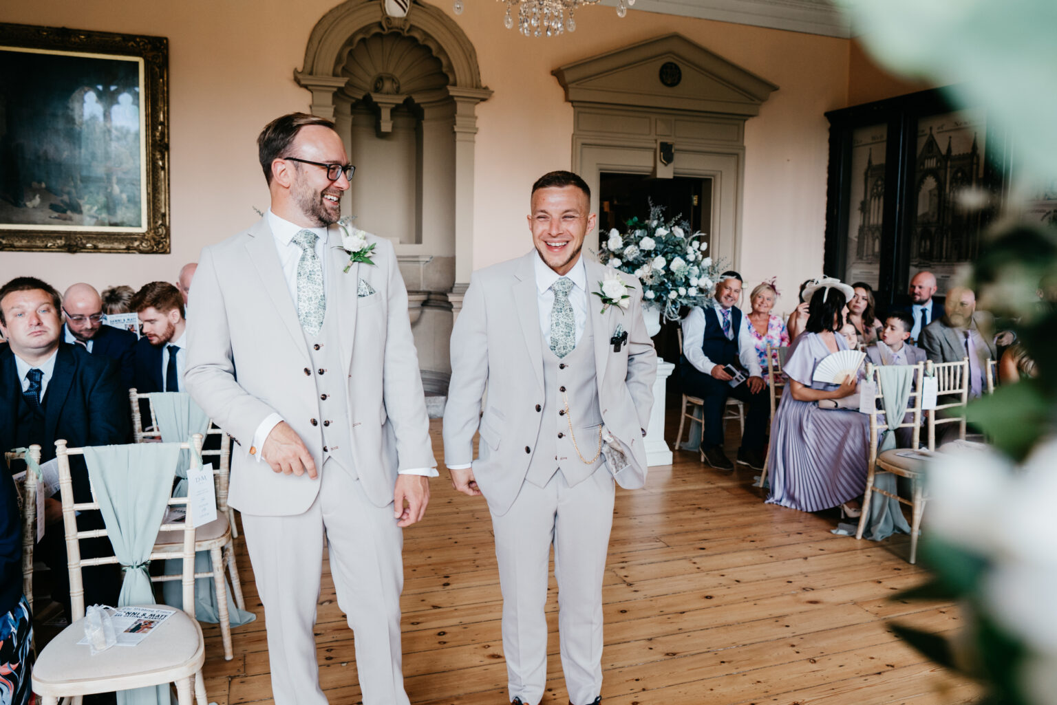Two grooms smiling at indoor wedding ceremony.
