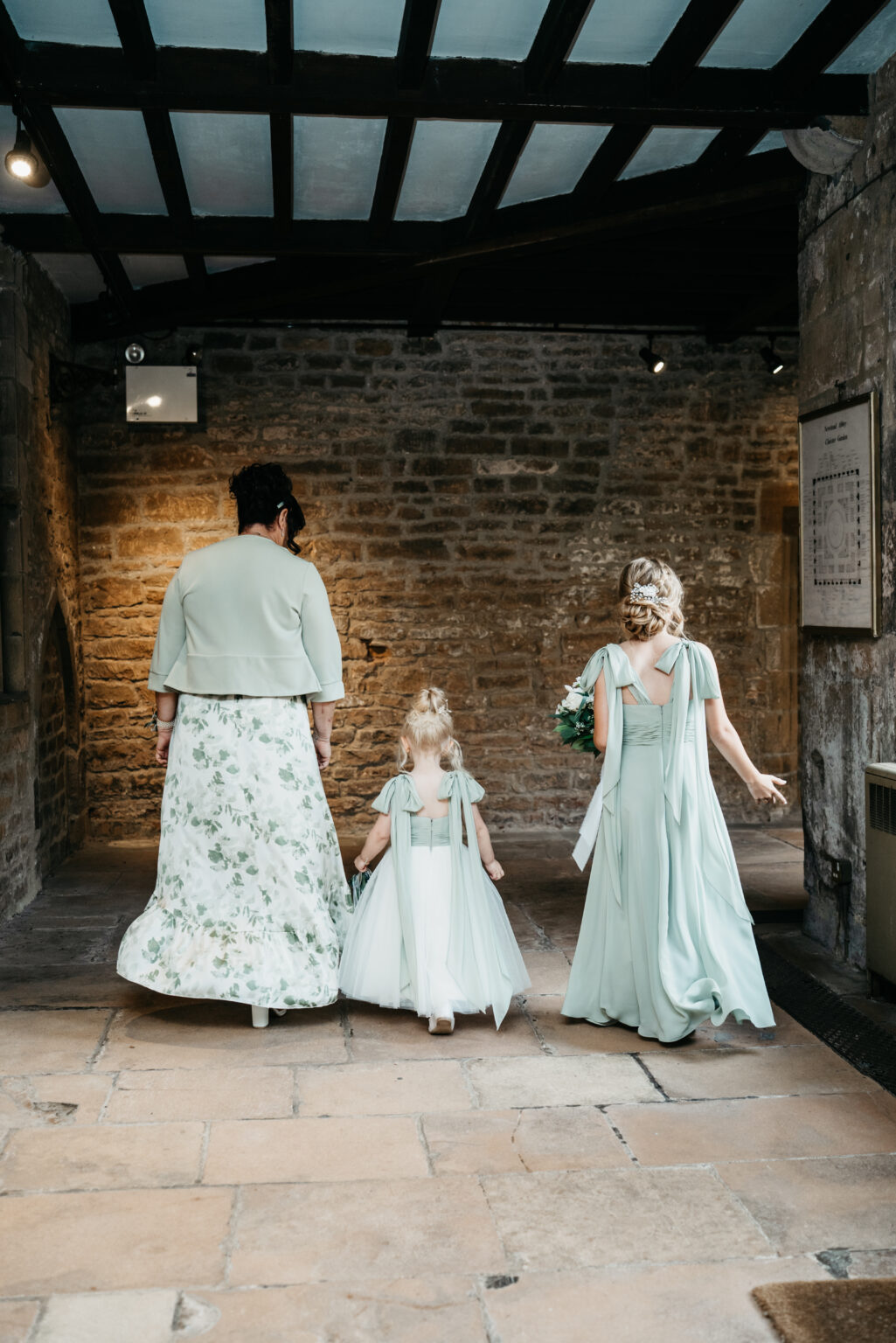Three bridesmaids in green dresses walking indoors.