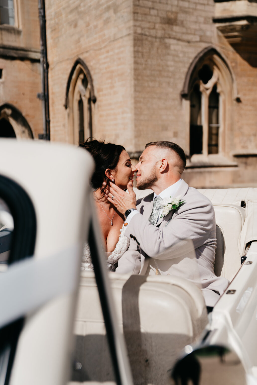 Bride and groom share romantic kiss in car.