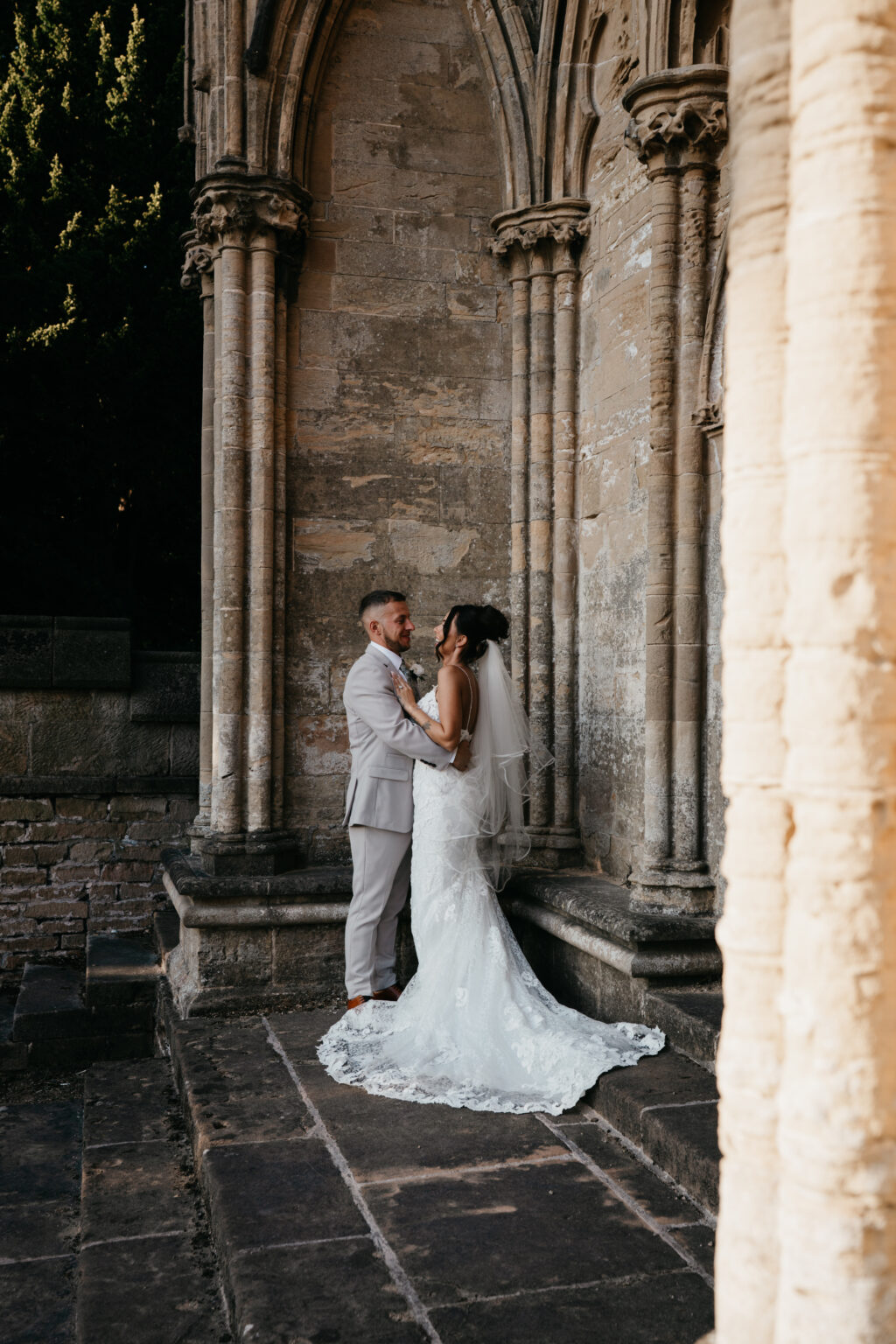 Bride and groom embrace near historic stone columns.