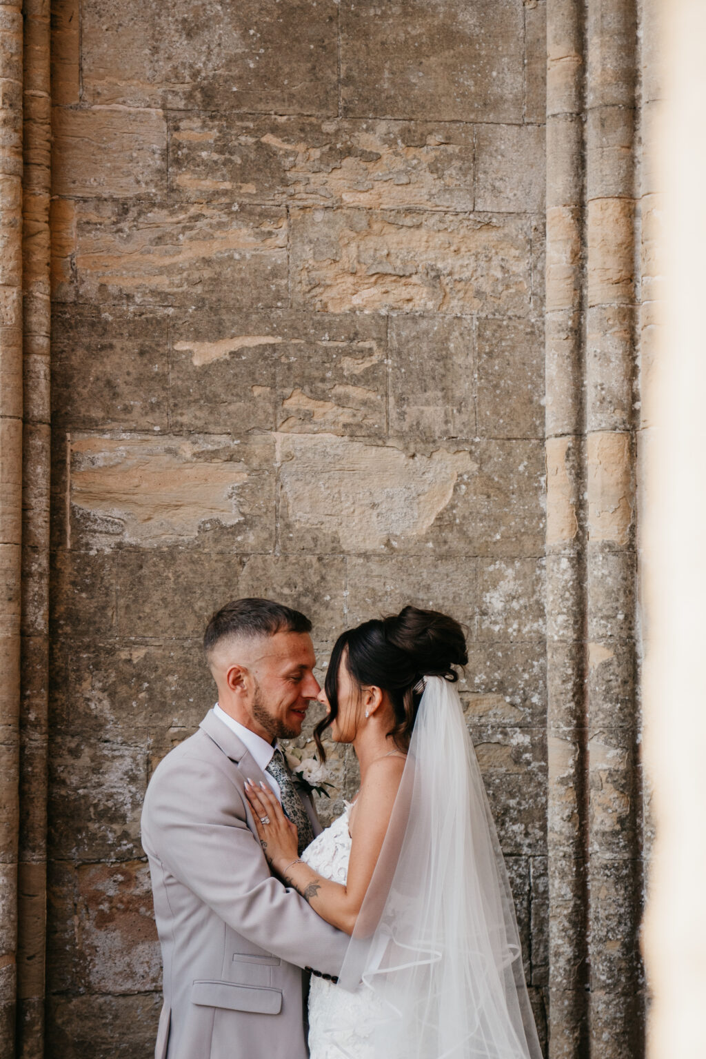 Bride and groom embracing near stone wall.