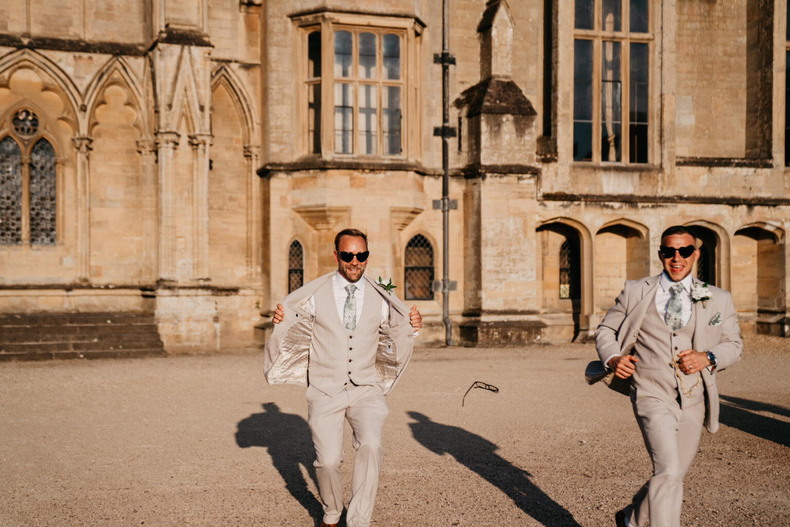 Two groomsmen laughing and running outside a historic building.