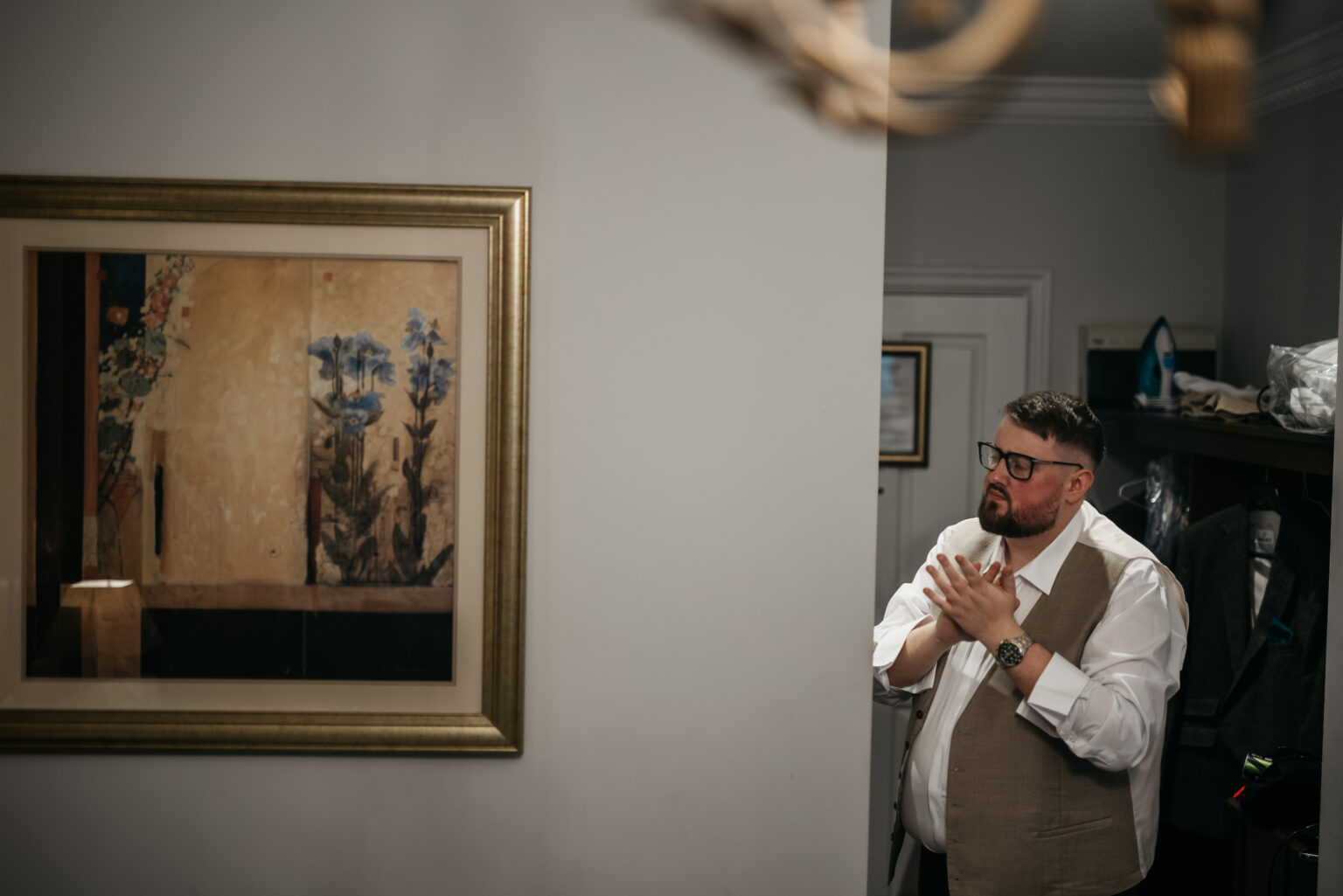 Man standing beside painting, adjusting clothes.