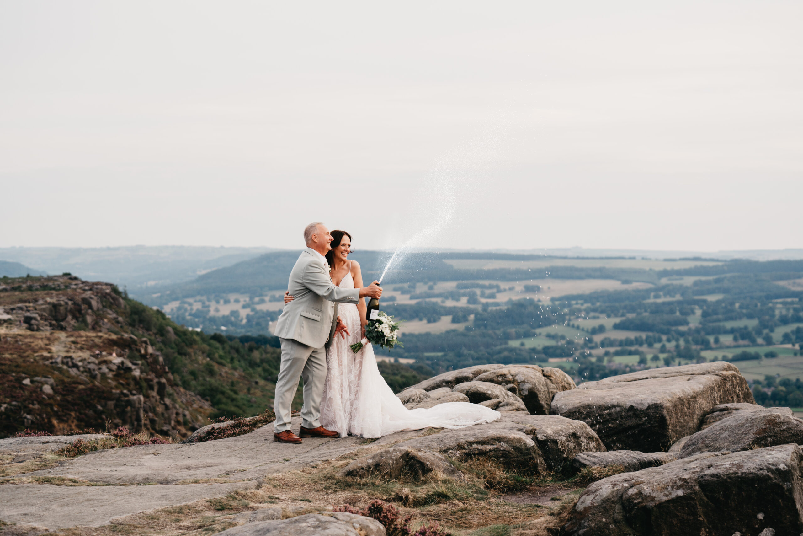 Bride and groom celebrating with champagne on cliff summit.